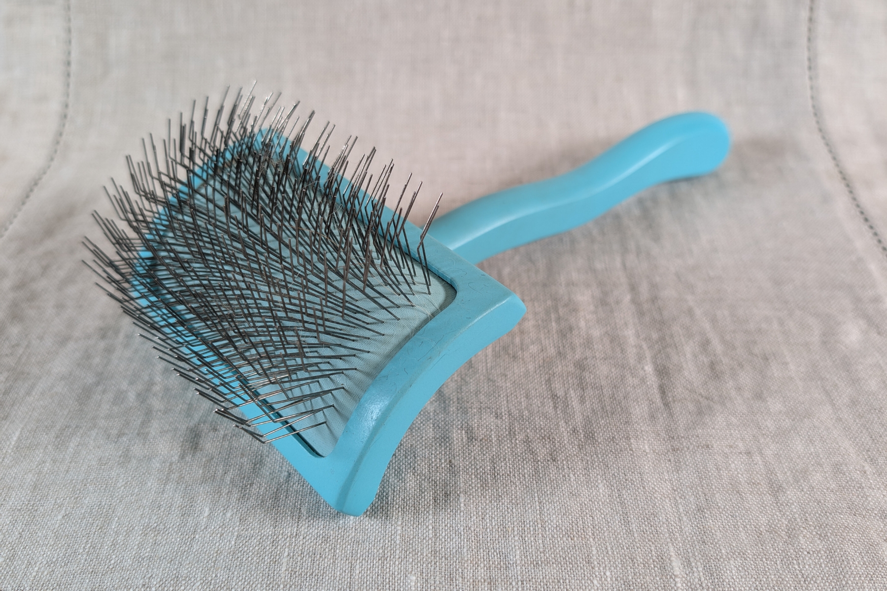 Chris Christensen Big G slicker brush resting on a linen cloth, its long metal pins in full view